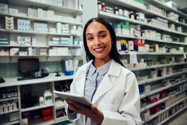 istock Happy woman working in pharmacy using digital tablet wearing labcoat looking at camera 1315972978
