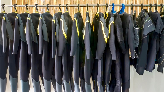 A row of black neoprene dive wetsuits hanging on a rack in a resort dive shop.
