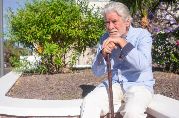 istock Suffering sad senior man sitting outdoors using a stick for legs pain 1315979655