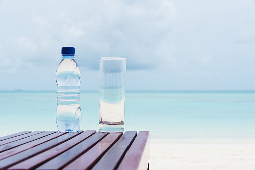 Bottle of mineral water and glass on the beach table