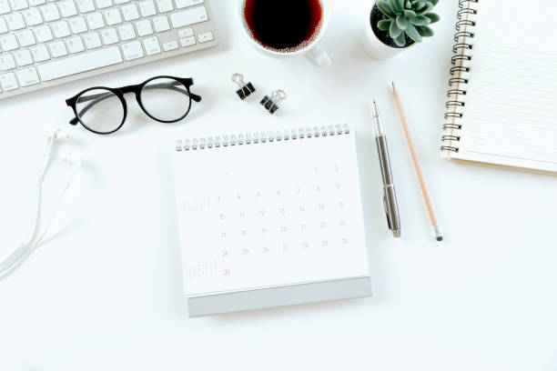 istock Modern white office desk table with computer, calendar, notebook, tree, glasses and cup of coffee. Top view with copy space, 1315983644