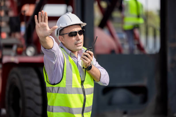 istock Man Using Walkie Talkie At Container Terminal, Industrial worker is controlling container loading 1315984257