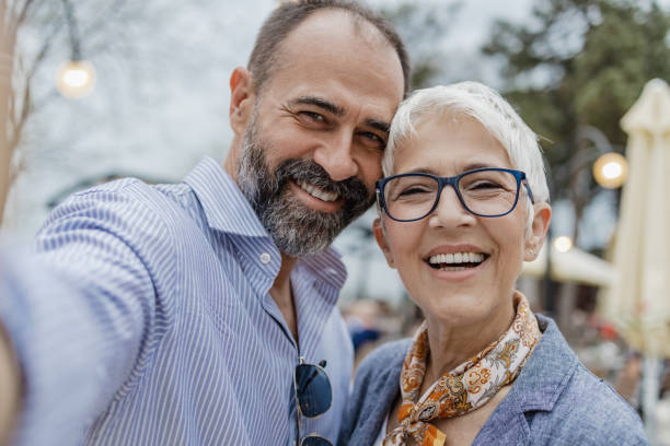 Cheerful mature couple is taking selfie. POV A cheerful mature couple on the street, they are taking a selfie age contrast stock pictures, royalty-free photos & images