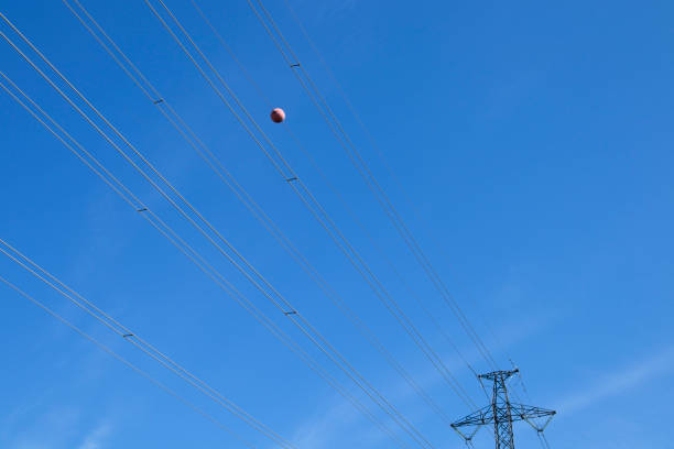 Single orange warning sphere on electric line against blue sky
