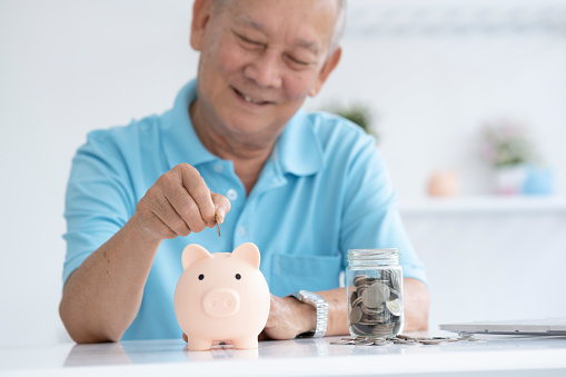 Elder man smiling putting a coin inside piggy bank as savings for investment and retirement saving planing.