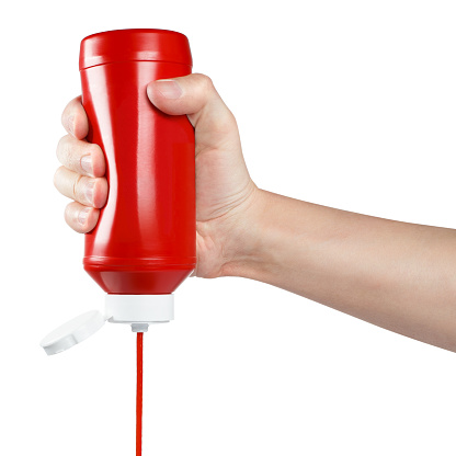 Hand squeezing ketchup out of a plastic bottle, isolated on white background