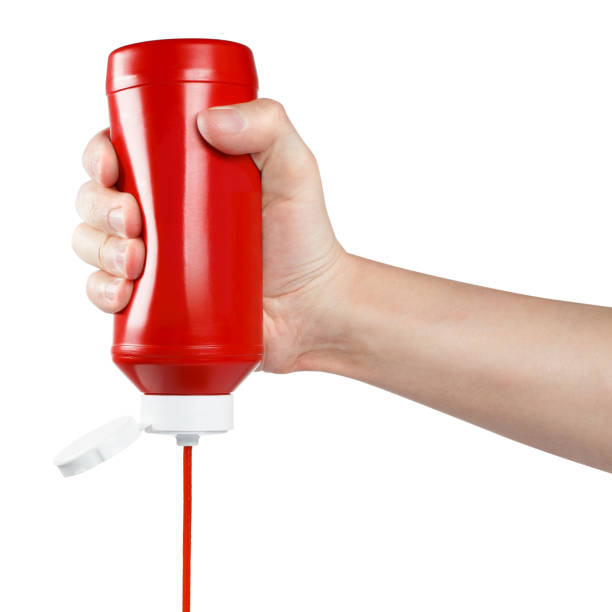 Hand squeezing ketchup out of a plastic bottle on white Hand squeezing ketchup out of a plastic bottle, isolated on white background ketchup bottle squirt stock pictures, royalty-free photos & images