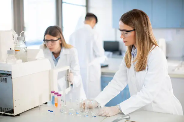 Photo of Female scientists in a white lab coat putting vial with a sample for an analysis on a ionchromatography system in biomedical lab