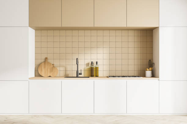 istock Front view of modern kitchen interior with kitchenware. Parquet floor. White facades and beige ceramic tiles on wall 1316011726