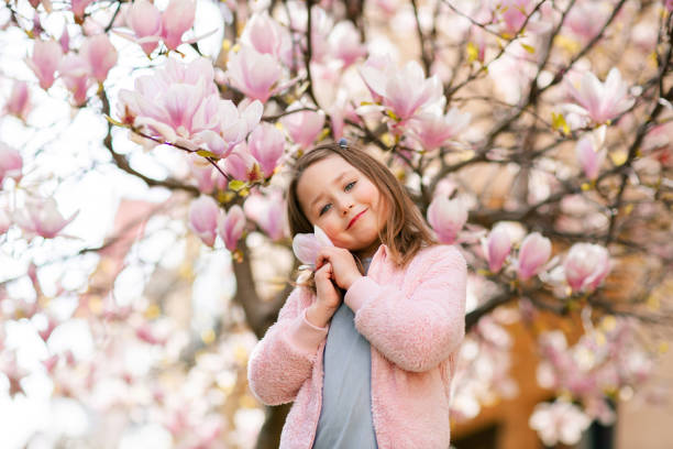 piękna uśmiechnięta dziewczynka w wiosennym ogrodzie w pobliżu kwitnącego drzewa magnolii - sweet magnolia tree blossom white zdjęcia i obrazy z banku zdjęć