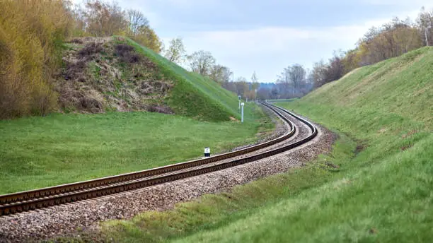 Photo of Selective focus railway track twists and turns between hills. Empty rounding and turning single track of railways. Shallow focus perspective view of rounded rails bend horizontal.