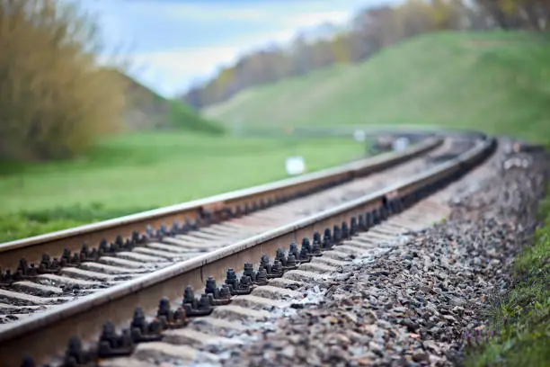 Photo of Selective focus railway track turns and twists between hills. Empty rounding and turning single track of railways. Shallow focus perspective view of rounded rails bend horizontal.