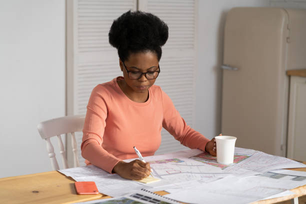 la mujer arquitecta concentrada dibuja el trabajo del plano en casa. diseñadora negra crea plan de proyecto - built structure coffee blueprint engineering fotografías e imágenes de stock