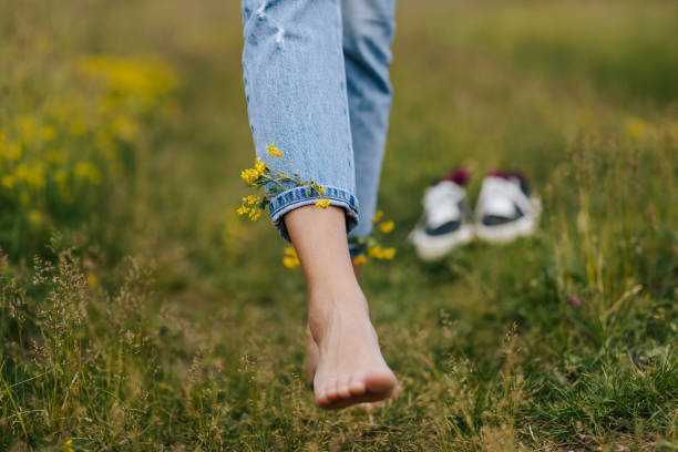 Close-up young female legs walking on green spring grass with wildflowers in legs of denim trousers