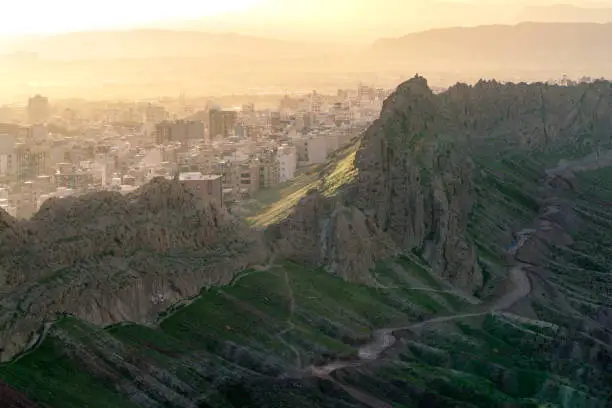 City of Qom, Iran, in a dramatic sunset viewed from the hill nearby. Steep rock cliffs in the front. Desert rocks, dramatic terrain. Persia.