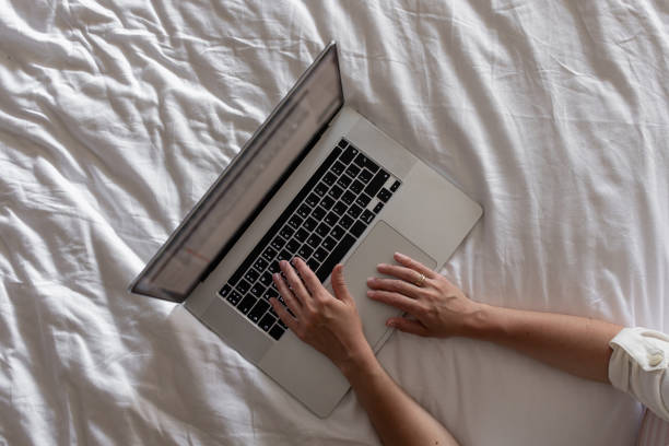 A young pregnant woman is seated cross-legged on a vibrant green couch, focused on her laptop. She appears relaxed and engaged, balancing work and her impending motherhood in a cozy home setting.