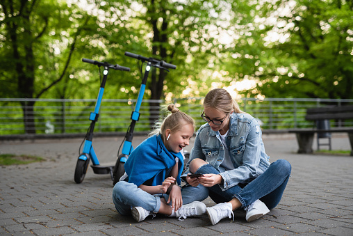Mother and daughter using application on smartphone for sharing electric scooters in city park