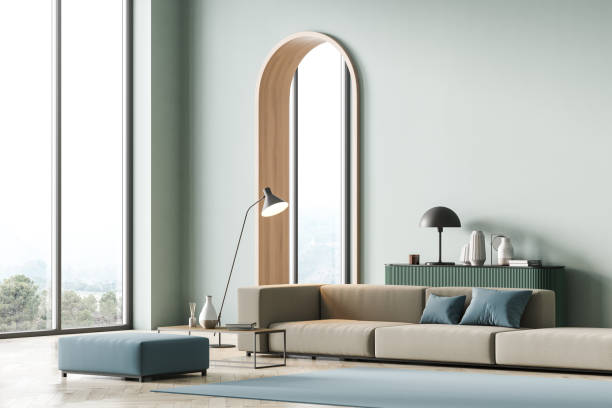 istock Modern living room interior with arch, mint color on wall and panoramic windows, hills view. Beige sofa with light blue cushions, coffee table, light green chest of drawers and lamp. Parquet floor. 1316019862