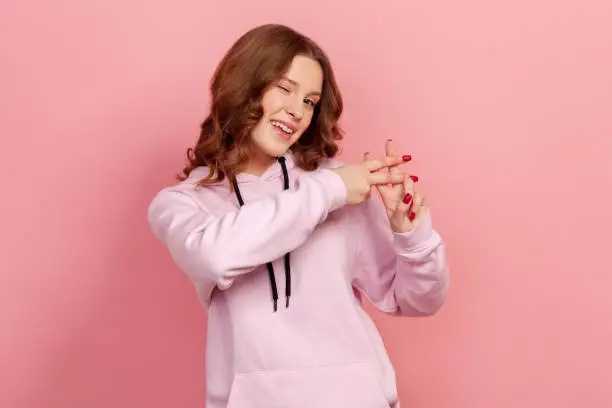 Photo of Portrait of cheerful curly haired teenage girl in hoodie showing hashtag symbol with fingers, smiling at camera, internet popularity