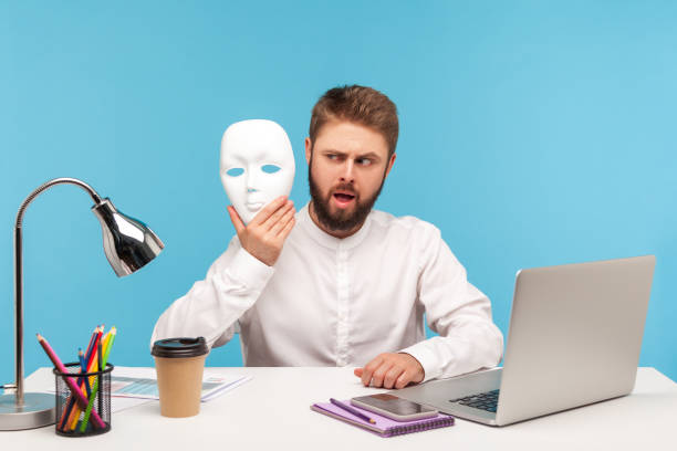 istock Bearded man office worker looking at white face mask in his hand with suspicion, hiding his identity, spying undercover, corruption 1316021817