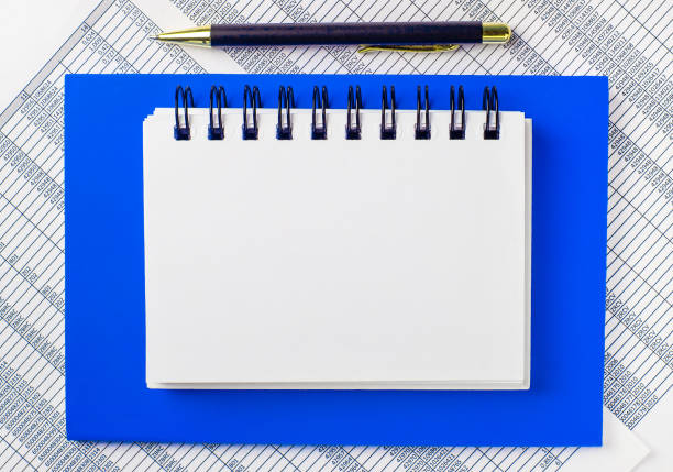 istock Against the background of reports on the desktop, a blue notepad. It has a pen and a clean white notebook with space to insert text. Template. Business concept 1316022124