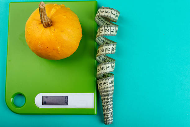 green scales with a pumpkin and a twisted centimeter. the concept of proper nutrition and diet. - textile healthy eating instrument of measurement tape measure imagens e fotografias de stock