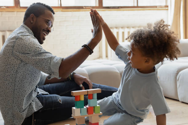 Happy millennial dad giving high five to toddler son Happy millennial dad giving high five to toddler son, celebrating building pyramid from wooden blocks. Happy kid playing learning games with daddy on heat floor. Parent teaching child concept preschool photos stock pictures, royalty-free photos & images