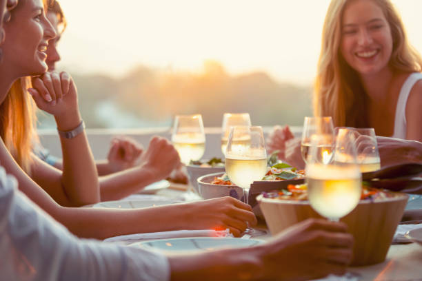 Group of friends drinking white wine at the table at a dinner party. Group of friends drinking white wine at the table at a dinner party. There are also bowls of other food and salad on the table. Time is sunset. Everyone is smiling and happy restaurant place setting dinner dinner party stock pictures, royalty-free photos & images