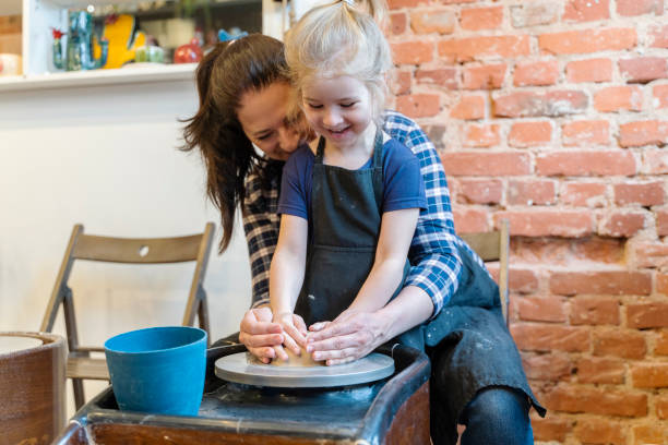 Happy Mother with adopted daughter and son. Teacher in Pottery workshop with two Children learning how to use clay for making beautiful dishes.