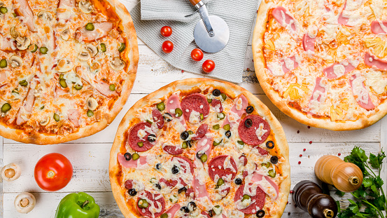 Italian meat pizza, hawaiian pizza, pizza with chicken and cheese top view on white wooden table with vegetables and spices