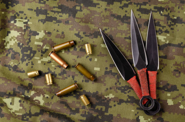 istock Black Throwing knives and casings on camouflage cloth. 1316040830