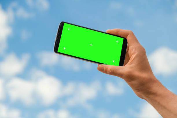 A phone with a green screen against a background of the sky stock photo