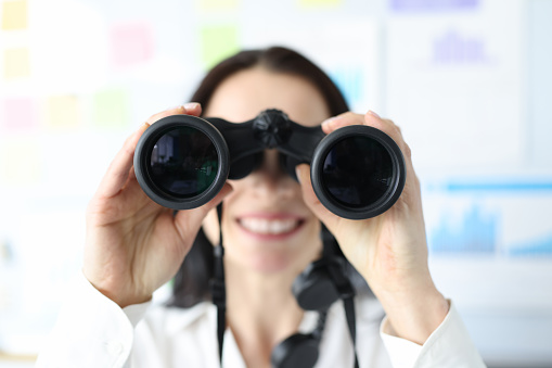 Woman looking in black professional binoculars in office closeup. Database search concept