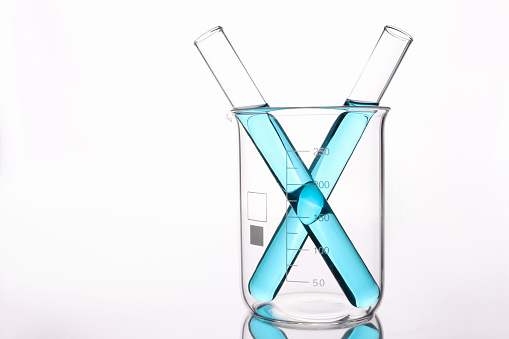 Two test tubes with blue acid standing in glass beaker on white background. Pharmaceutical industry concept