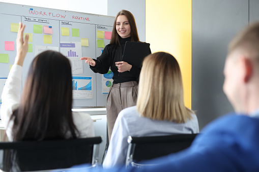 Woman business coach standing near blackboard and asking question to listener. Educational business seminars concept