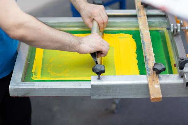 istock Serigraphy silk screen print process at clothes factory. Frame, squeegee and plastisol color paints 1316050350