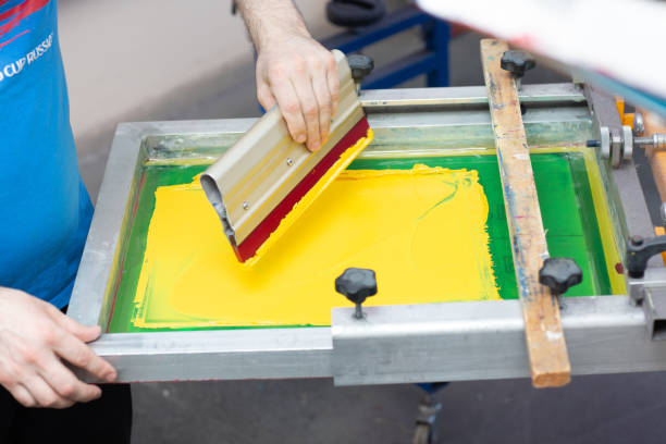 istock Serigraphy silk screen print process at clothes factory. Frame, squeegee and plastisol color paints 1316050356