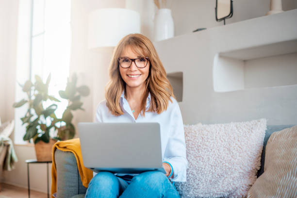 istock Happy middle aged woman using her laptop while sitting on the sofa at home 1316051422