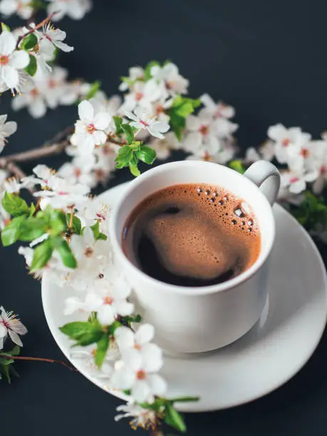 Photo of Close-up of a cup of fragrant coffee on the table with branches of a blooming white cherry. Spring time