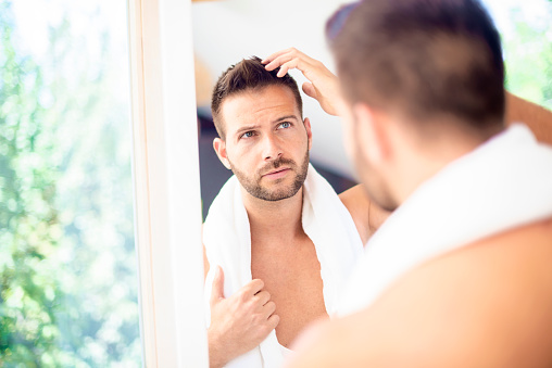 Close-up shot of a handsome young man with towel in his neck while doing his hair in the bathroom mirror.