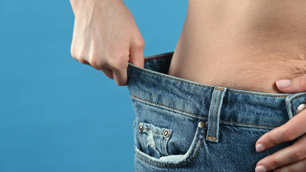 A woman shows that her jeans are too big The concept of overweight, weight loss, diet, obesity, junk food. A woman shows that her jeans are too big The concept of overweight, weight loss, diet, obesity, junk food. High quality photo too thin stock pictures, royalty-free photos & images