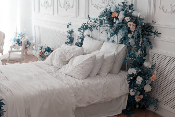 белая спальня. большая удобная двуспальная кровать украшена пурпурными листьями и цветами. спальня в мягких светлых тонах. кровать молодож - pillow bedroom bed rural scene стоковые фото и изображения