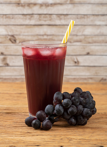 Red grape juice in a glass with ice and fruits over wooden table.