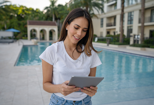 Portrait of a Real Estate Agent at a luxurious property with a swimming pool and working online using a tablet computer