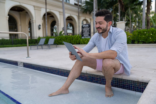 istock Happy man on vacation watching photos on his tablet while sitting by the pool 1316069407