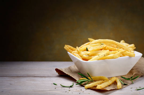 French fries and fresh rosemary on wooden table, copy space. Homemade potato chips in ceramic bowl. fried potato stock pictures, royalty-free photos & images