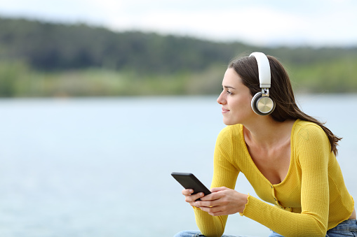 Satisfied woman listening to music with wireless headphones looking away in a lake