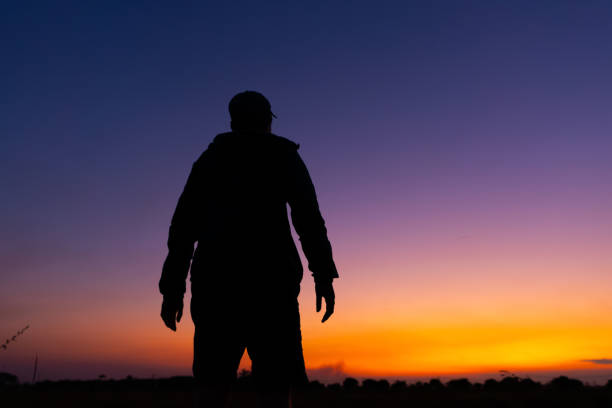 silhouette dark young man wearing a hat standing emotions with evening Twilight sky with cloud in the winter season at sunset Abstract background.Copy space for your