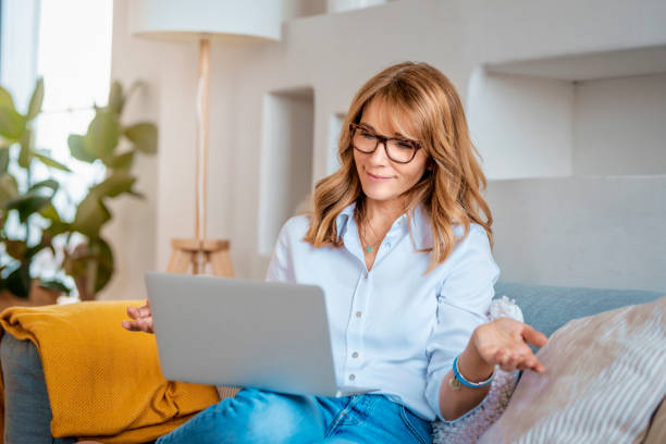 istock Happy middle aged woman using her laptop and having video call while sitting on the sofa at home 1316076391