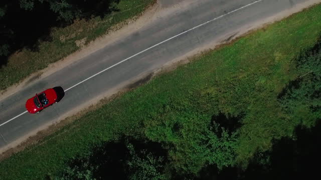 Aerial view of red car driving on country road in forest.